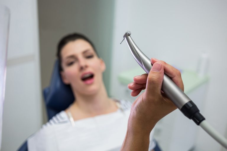 Close-up of dentist holding a dentistry, dental handpiece while examining a woman at clinic