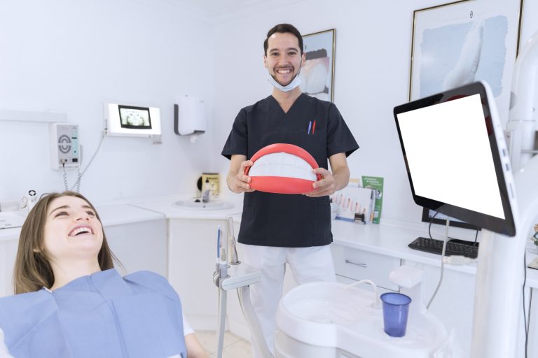 happy-male-dentist-holding-big-teeth-model-clinic