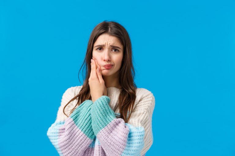 Health, stomatology concept. Silly cute woman in winter sweater, complaining on toothache, having decay or rotten tooth, touching cheek frowning and sulking from pain, waiting in dentist office