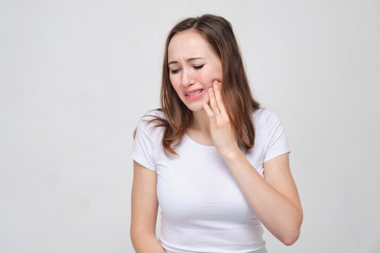 A portrait of a young girl in a white shirt holds his hand at his cheek. The concept of toothache. Close up.