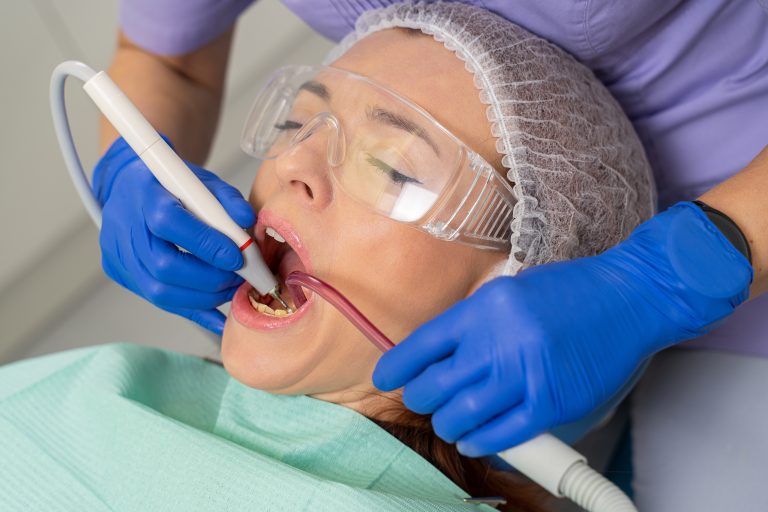 Close-up of a girl's patient at the moment when the dentist is using her ultrasound and saliva pump to clean her teeth from tartar.